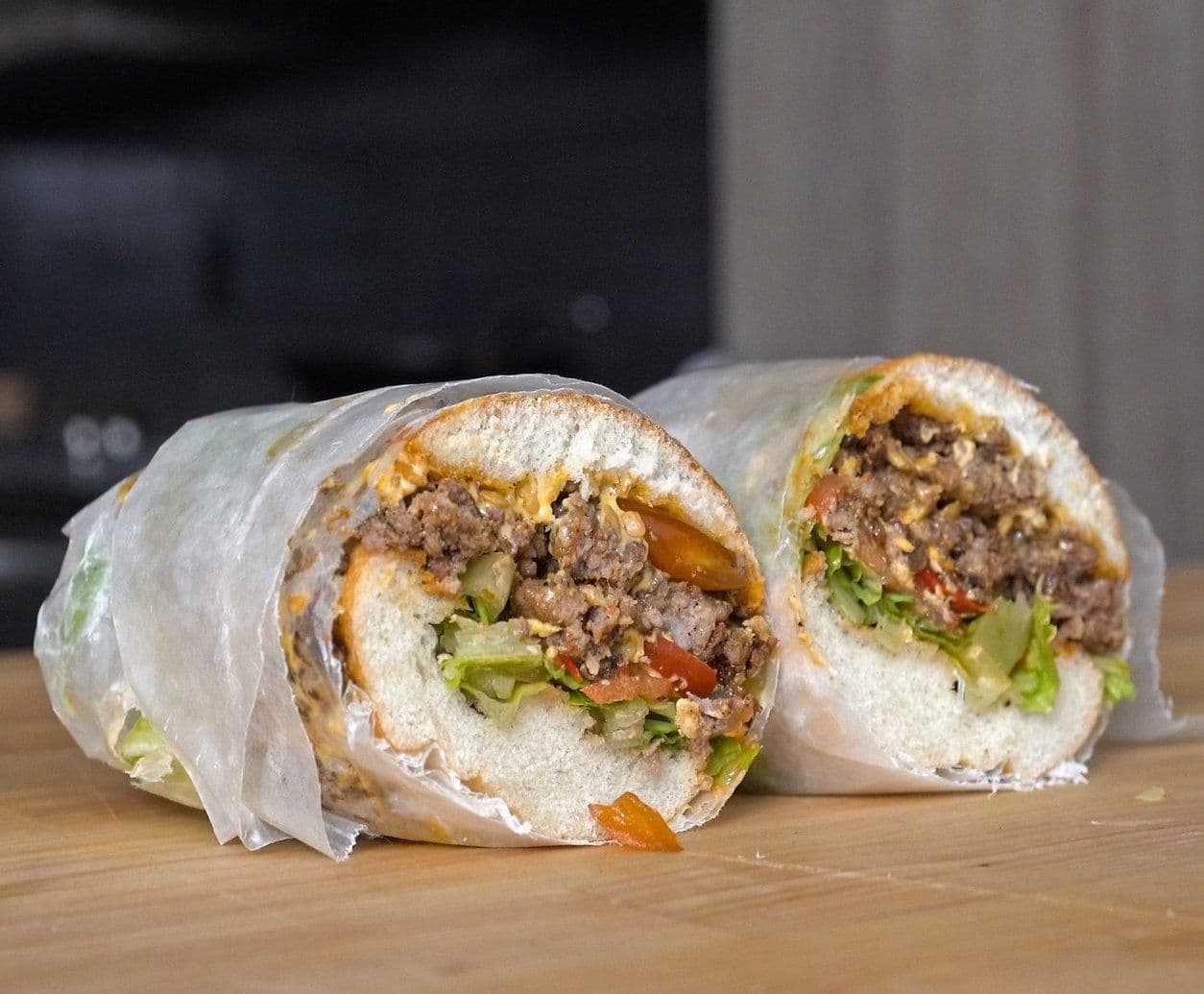 A hoagie roll stuffed with well browned meat, lettuce, tomato, and melted cheese